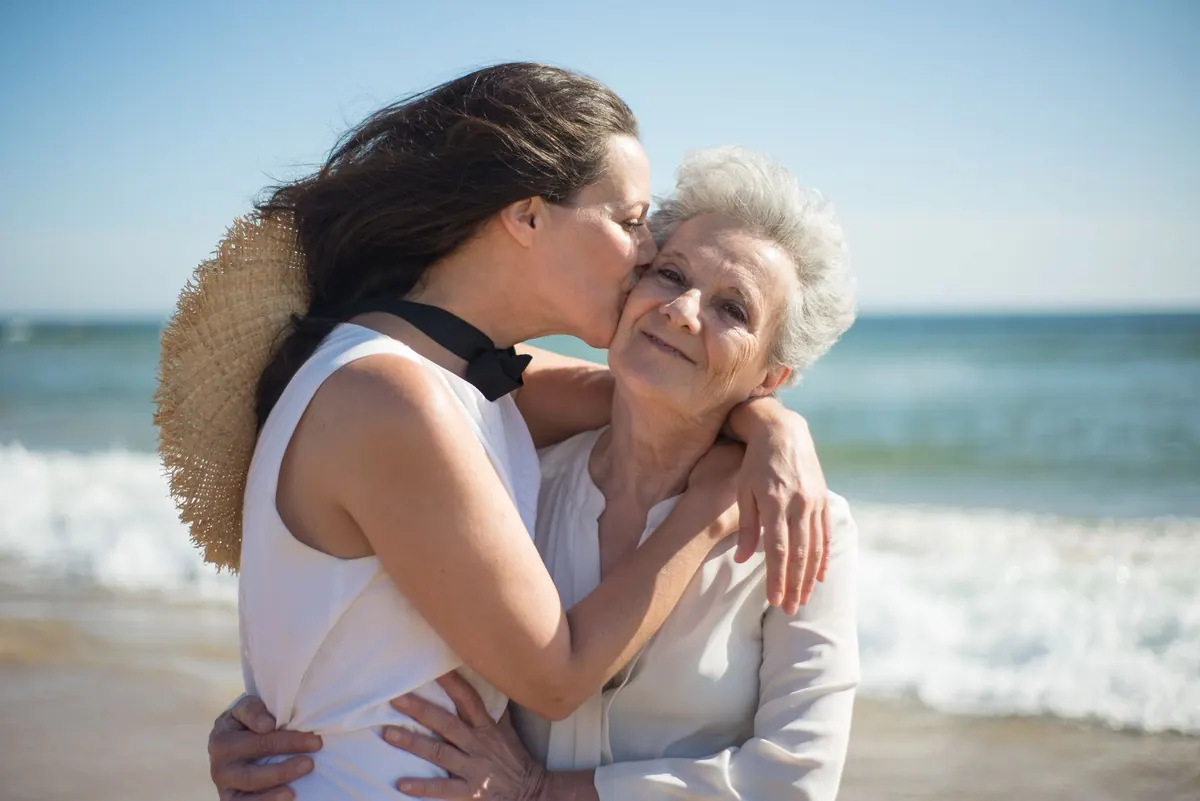 A mother and her adult daughter sharing a hug on the beach