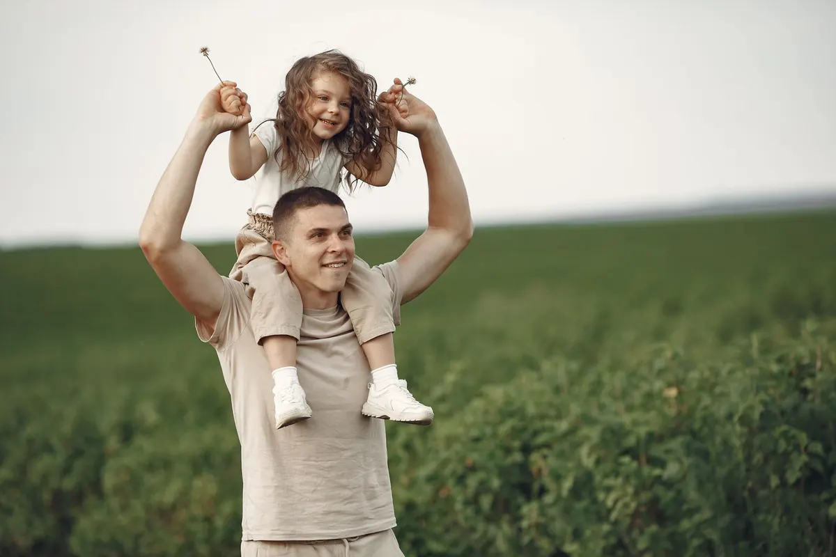 A father lifting his daughter onto his shoulders in a green field