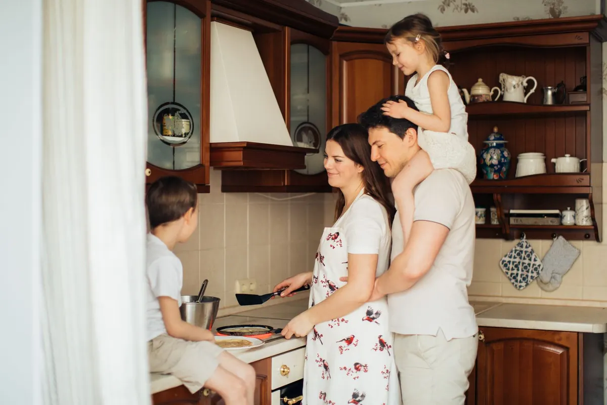 A family cooking together in their kitchen, their daughter on dad's shoulders