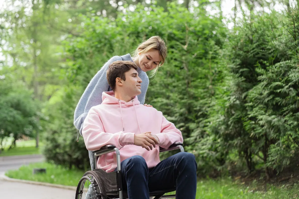 A young man in a wheelchair and his partner sharing a laugh in a park