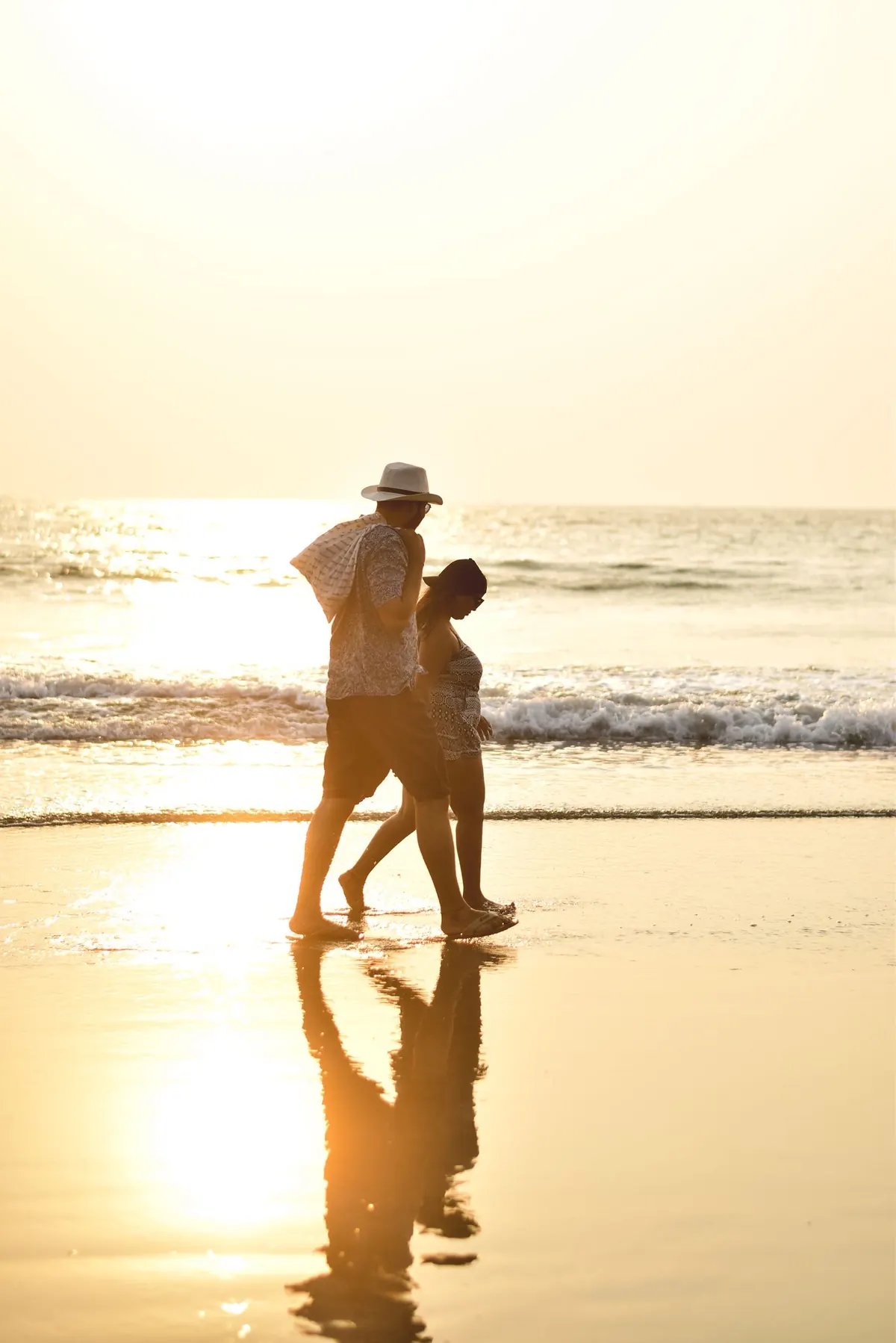 A couple walking hand in hand along the beach at sunset